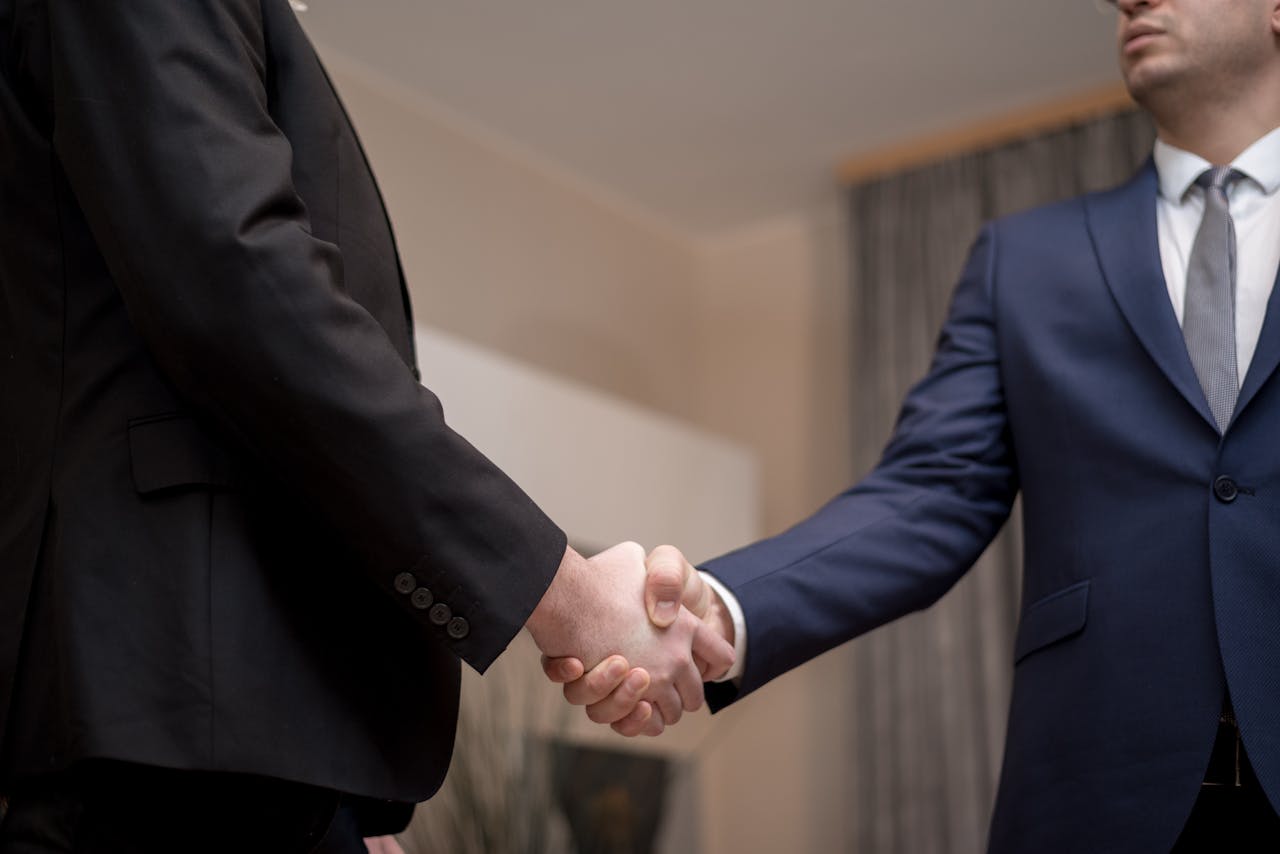 Two businessmen in suits shaking hands, emphasizing trust and partnership indoors.
